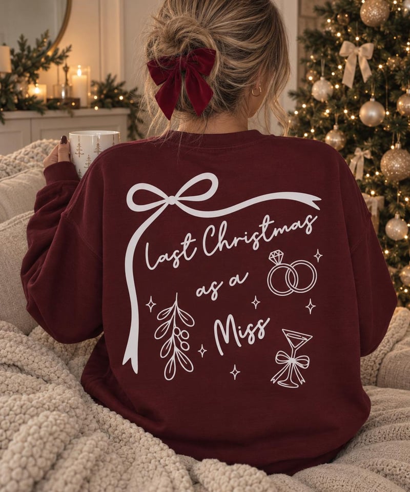 a woman sitting on a bed wearing a maroon coloured sweatshirt with festive white details on the back.