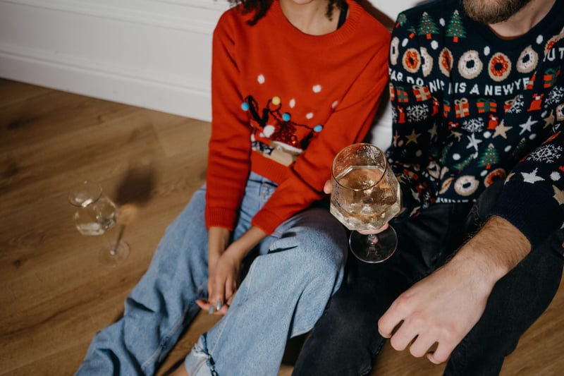 close up of a couple wearing Christmas jumpers and drinking Champagne.