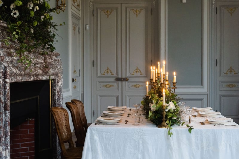 a grand fireplace and candlelit table covered with winter foliage arrangements.