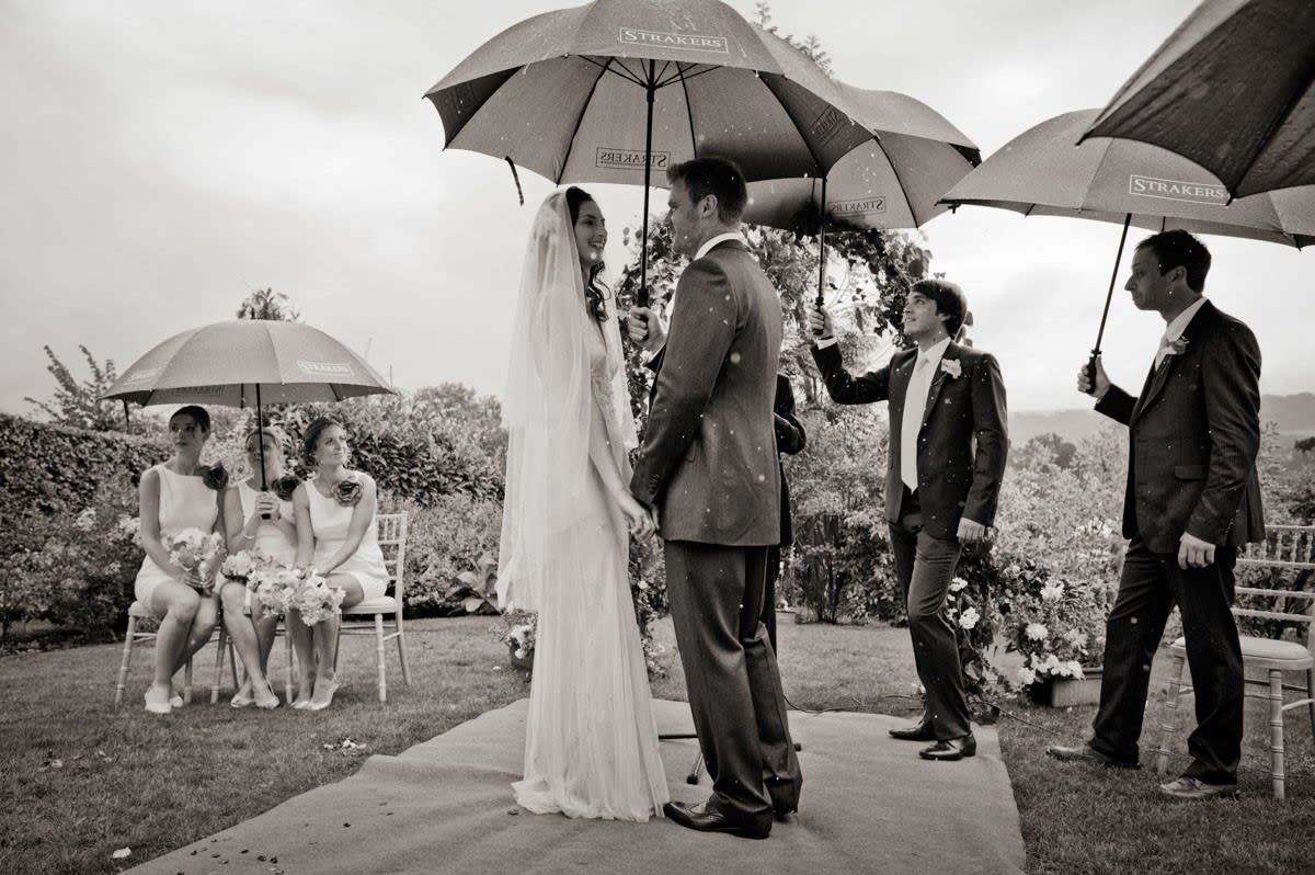 Bridebook.co.uk- bride and groom in outdoor ceremony under umbrellas