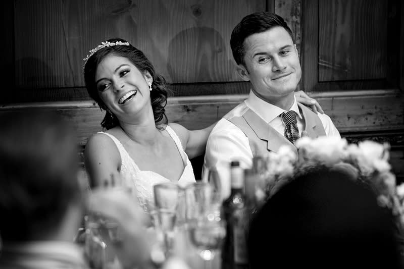 Bridebook.co.uk- bride and groom listening to speeches smiling