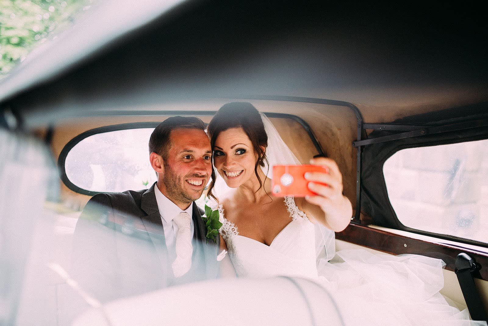 Bridebook.co.uk- bride and groom taking selfie at the back of wedding car