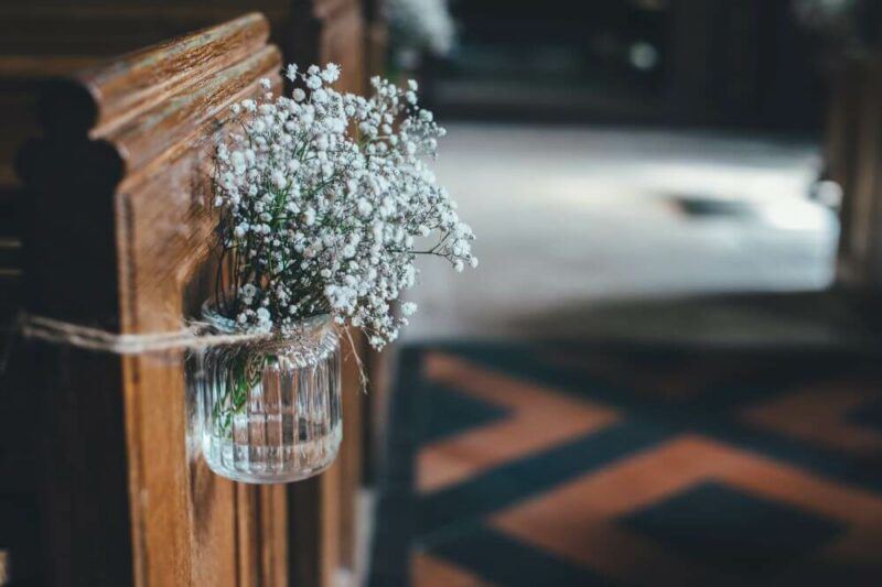 bridebook.com picture of a jar of baby's breath flowers tied to the side of a church pew