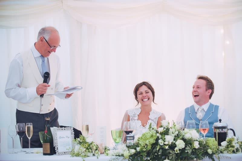  father of the bride reading his speech as bride and groom laugh