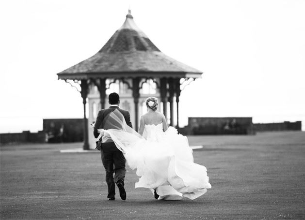 Bridebook.co.uk- and groom walking and bride skirt billowing in the wind