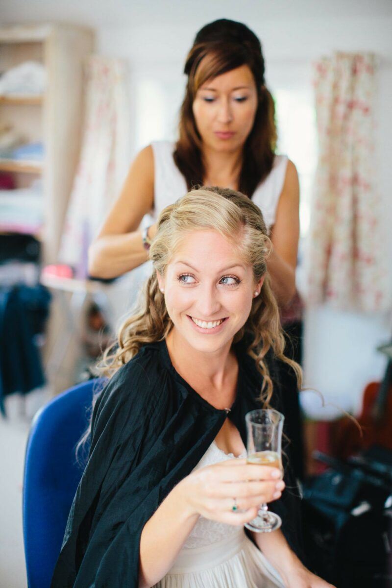 www.bridebook.co.uk bride having her hair done and drinking champagne