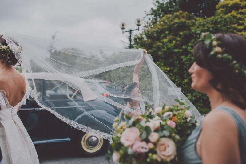 Bridebook.co.uk- brides cathedral length veil being adjusted by bridesmaid