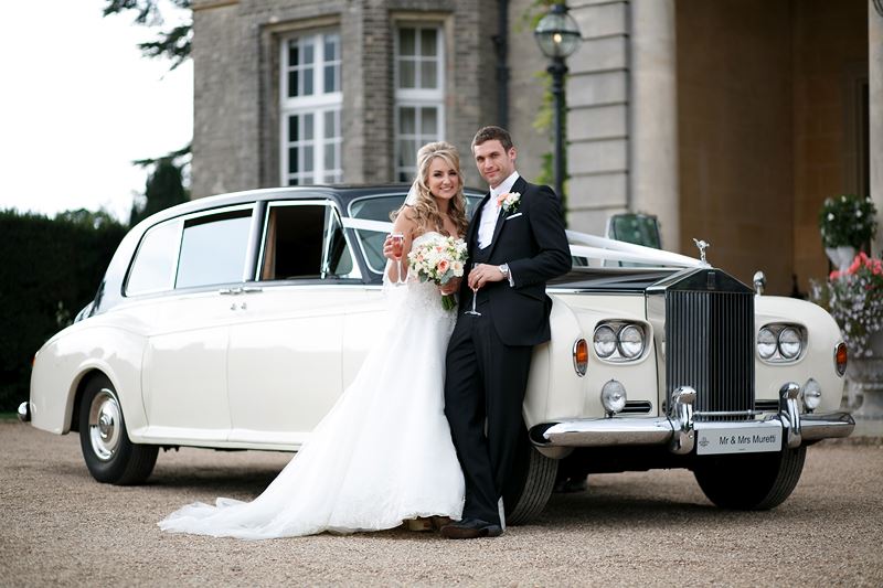 Bridebook.co.uk- couple posing for a photo in front of white wedding car