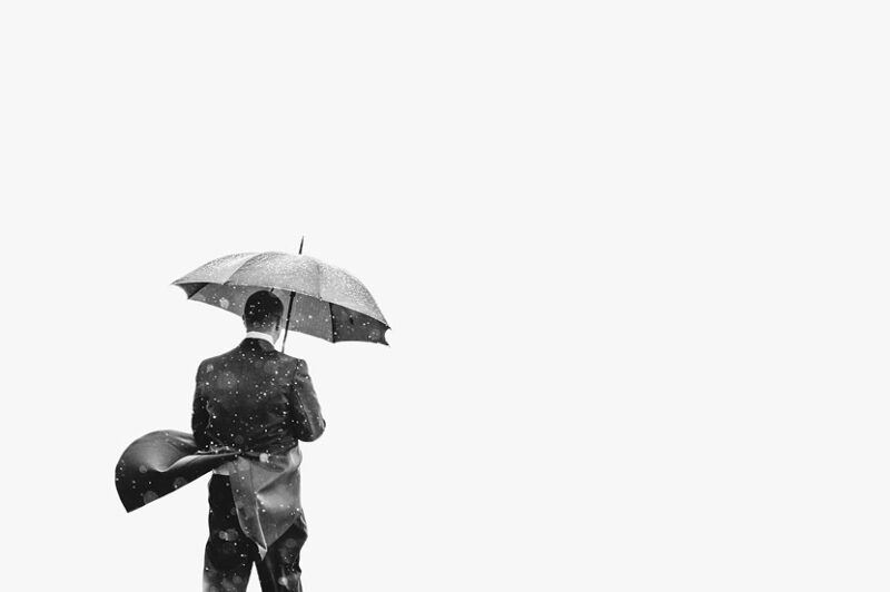 Bridebook.co.uk- groom standing under umbrella in the rain