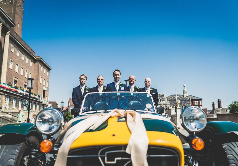 Bridebook.co.uk- groom and ushers standing in yellow sports car