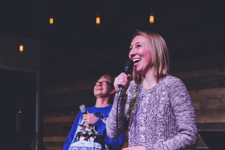 Smiling woman singing karaoke and laughing friend