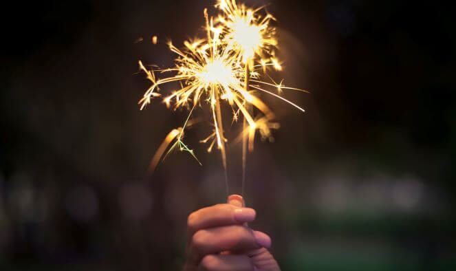 A hand holding two lit sparklers at night