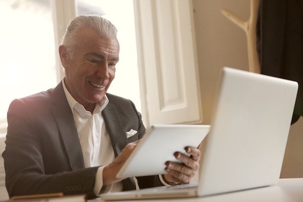 Älterer Mann lächelt mit Gadgets und Computer