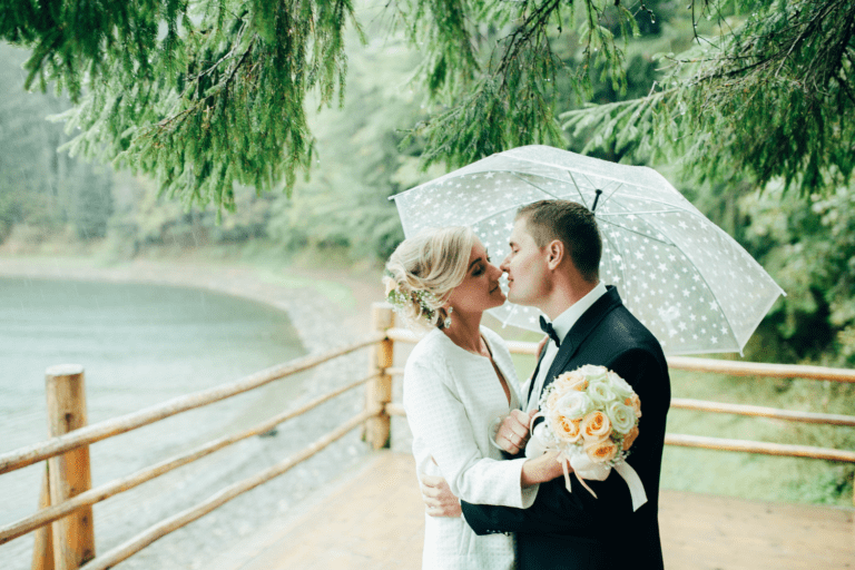 Bride and groom embracing in the rain under an umbrella