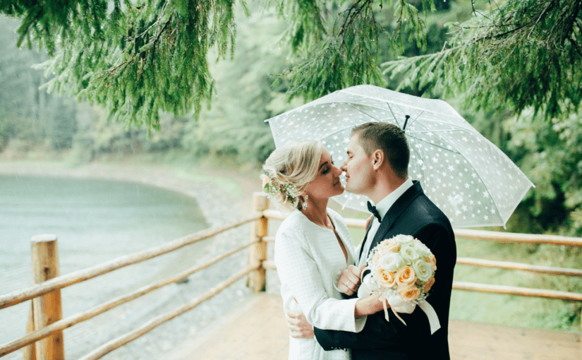 Bride and groom embracing in the rain under an umbrella