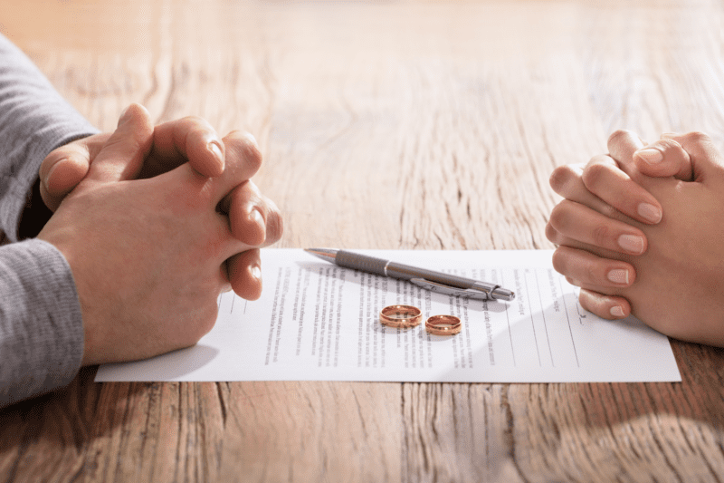 Couple signing a marriage contract with their wedding rings laid upon the document
