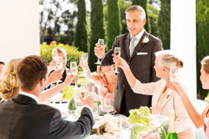 Father of the bride raising a glass to toast the bride and groom with other guests raising their glasses too