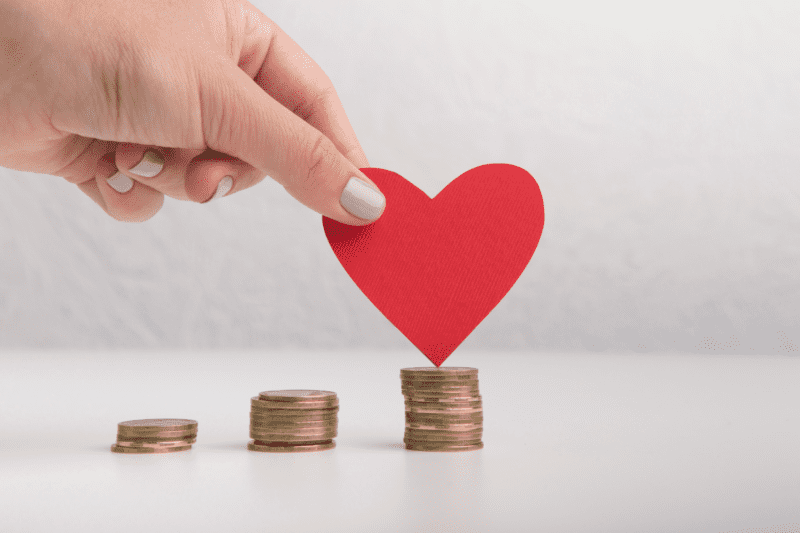 Piles of coins with a cut-out red paper heart