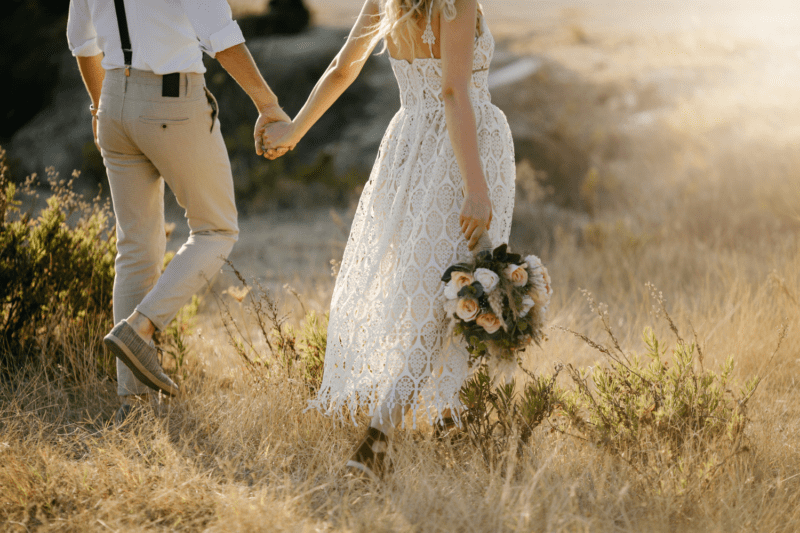 Bride and groom walking through wheat field hand in hand