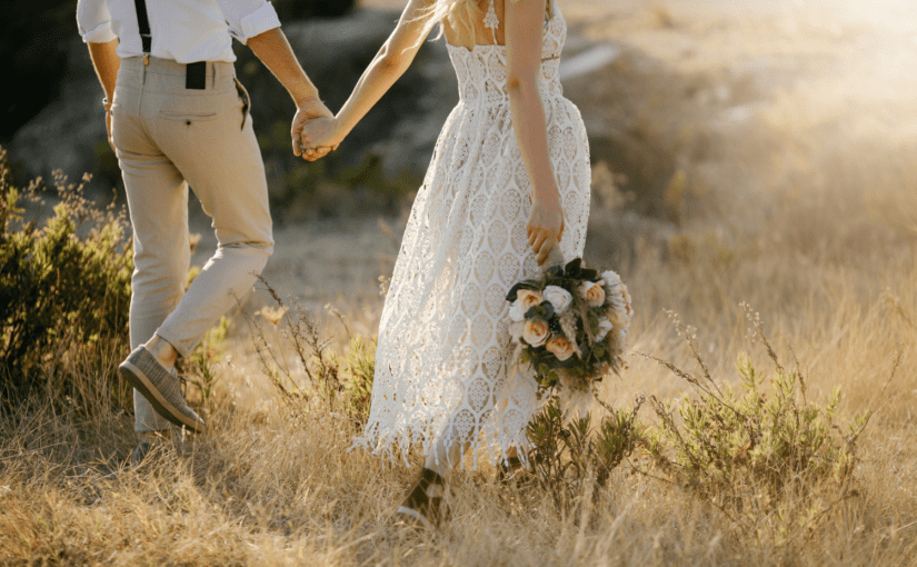 Bride and groom walking through wheat field hand in hand