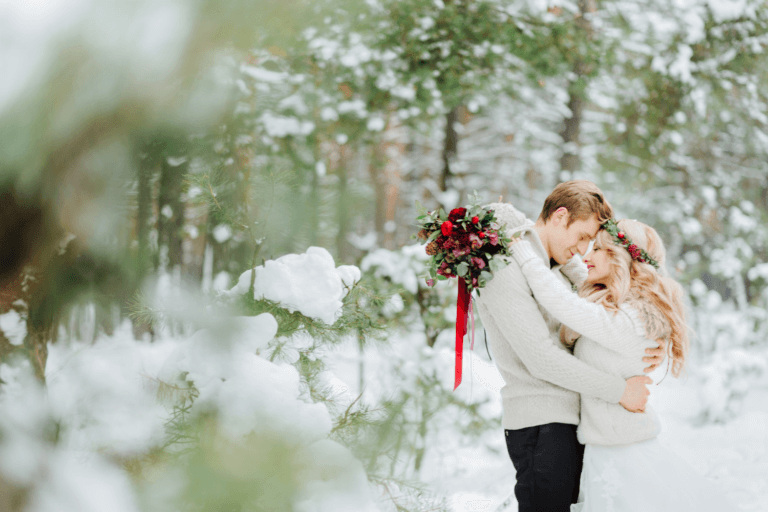 Bride and groom in an outdoor wintry setting with festive red garland and bouquet