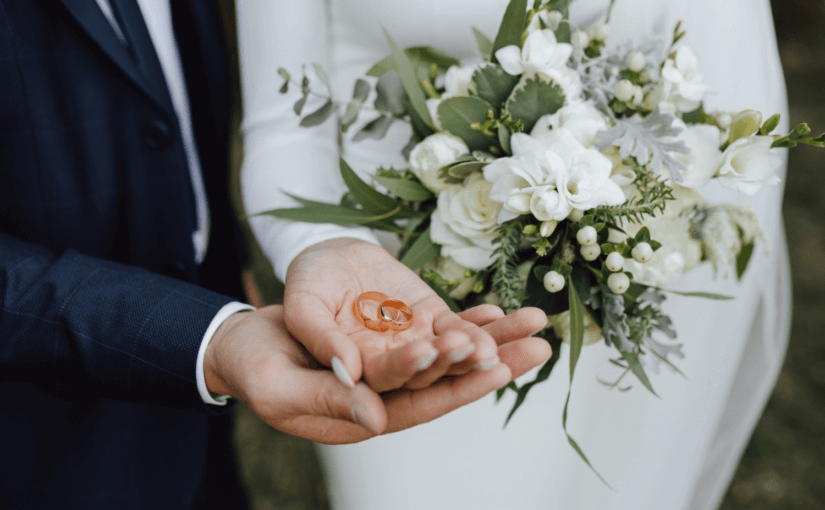Bride and groom holding two wedding rings in their hands and a white bouquet