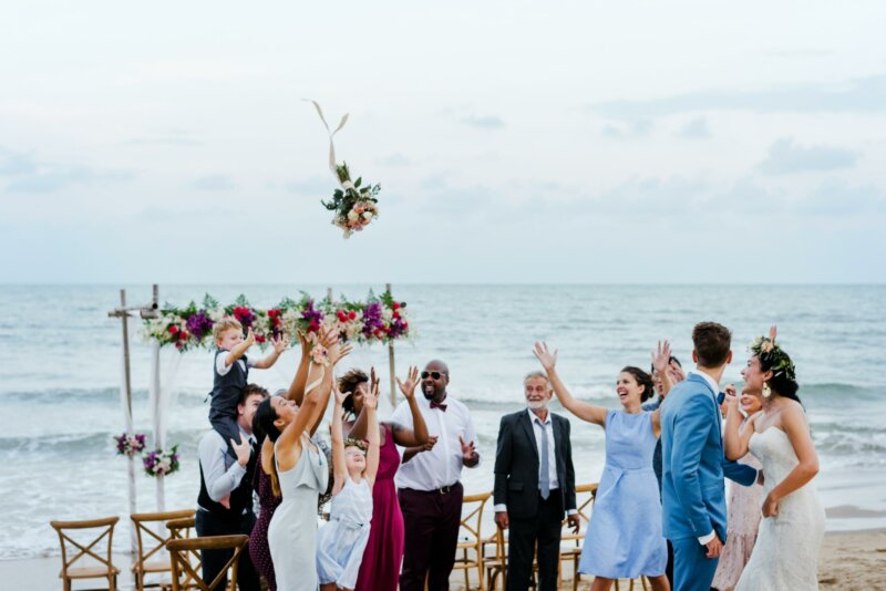 People trying to catch a bouquet at a beach wedding