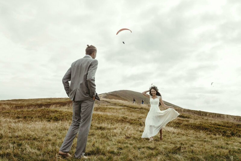 Newlywed couple in a field with a flying paraglider