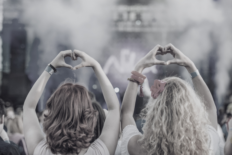 Deux femmes à un concert en train de faire un cœur avec leurs mains.