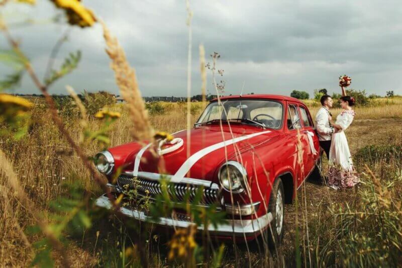 Couple de mariés derrière une voiture rouge