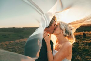 Kissing married couple at sunset with floating veil