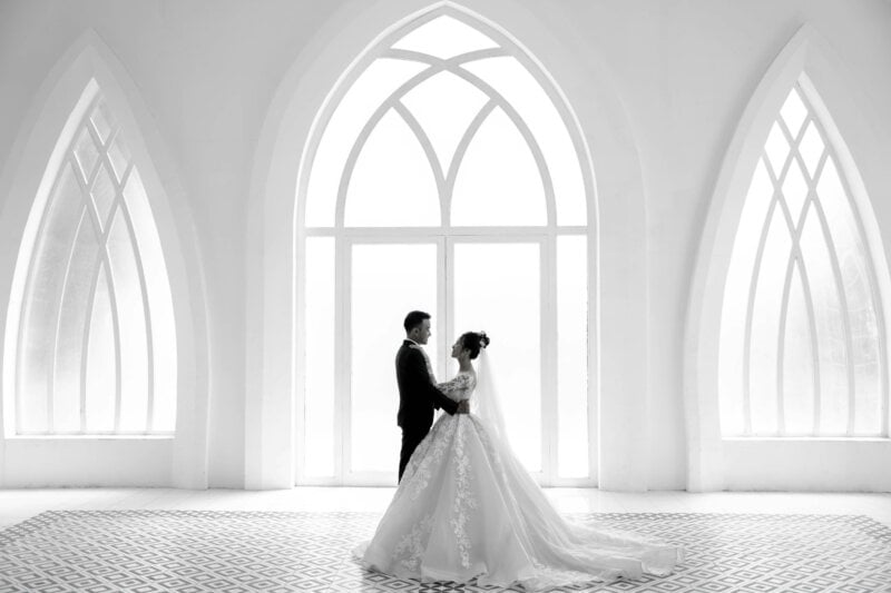 Couple de mariés en noir et blanc devant une fenêtre