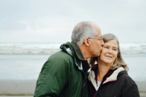 Älteres Paar küsst sich am Strand auf die Wange