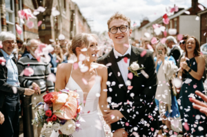 Bride holding a bouquet and groom walking down the aisle with petals in the air
