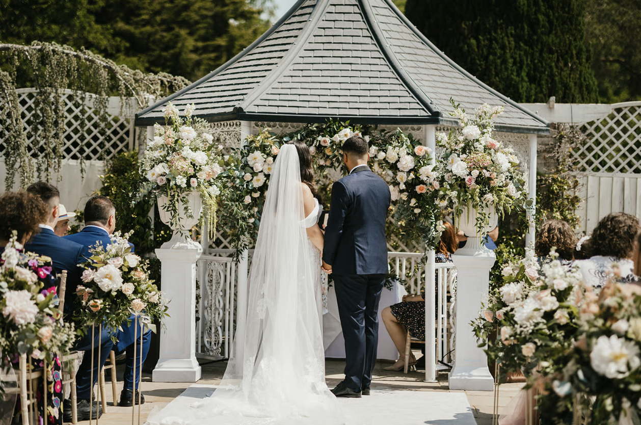 Bride and groom standing together during their outdoor ceremony surrounding by flowers