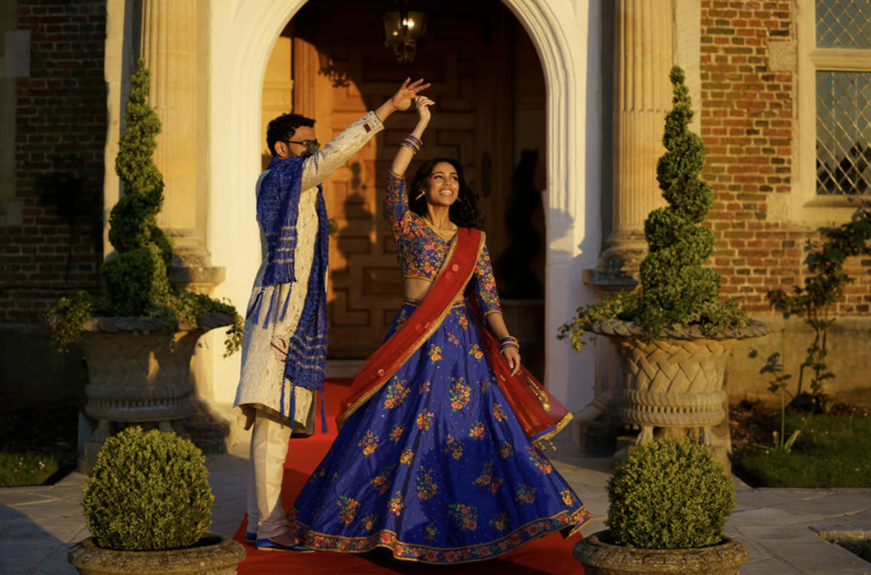 Newly wedded couple in traditional Indian wedding attire dancing outdoors during golden hour