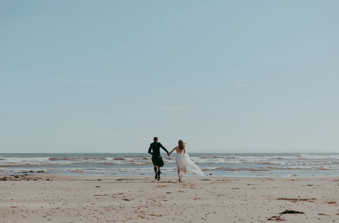 Newly wedded couple cinematically running on the beach