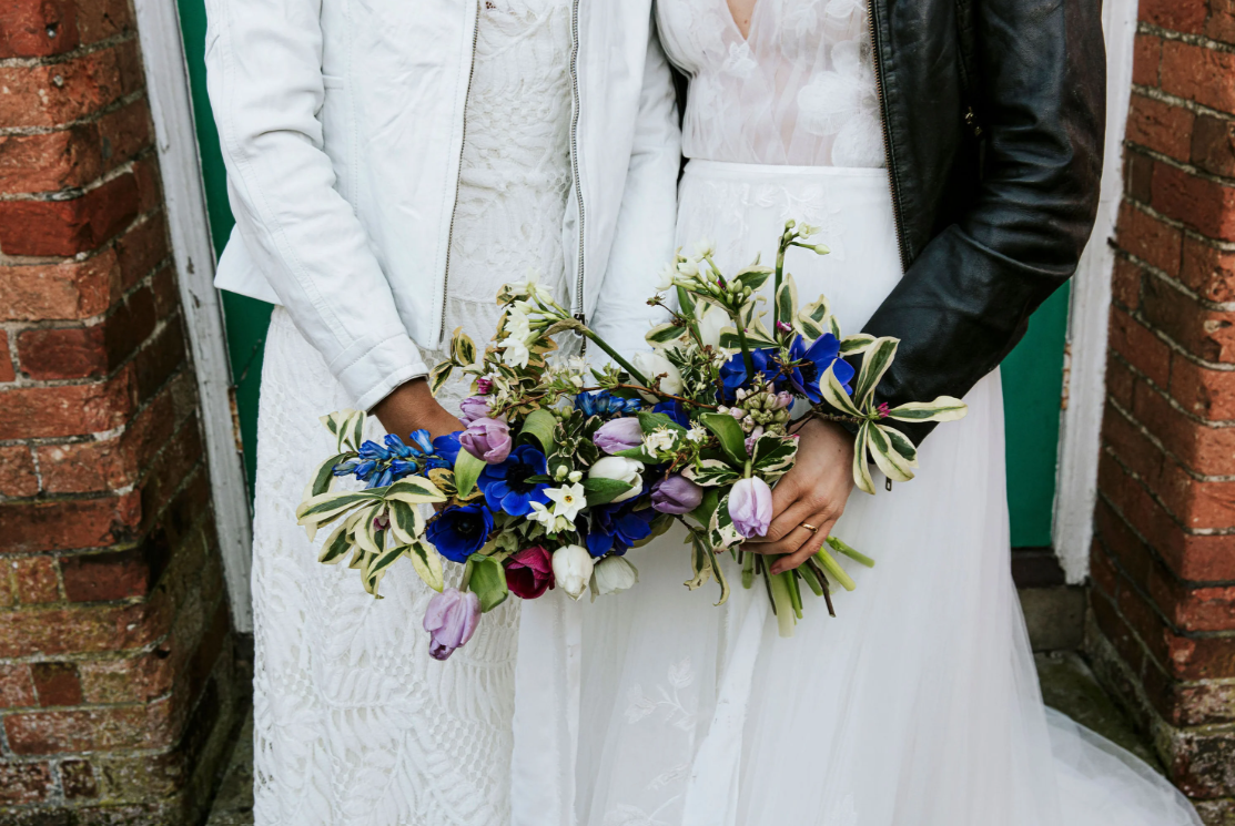 Detail shot of two brides in their wedding dress' and leather jackets holding flower bouquets
