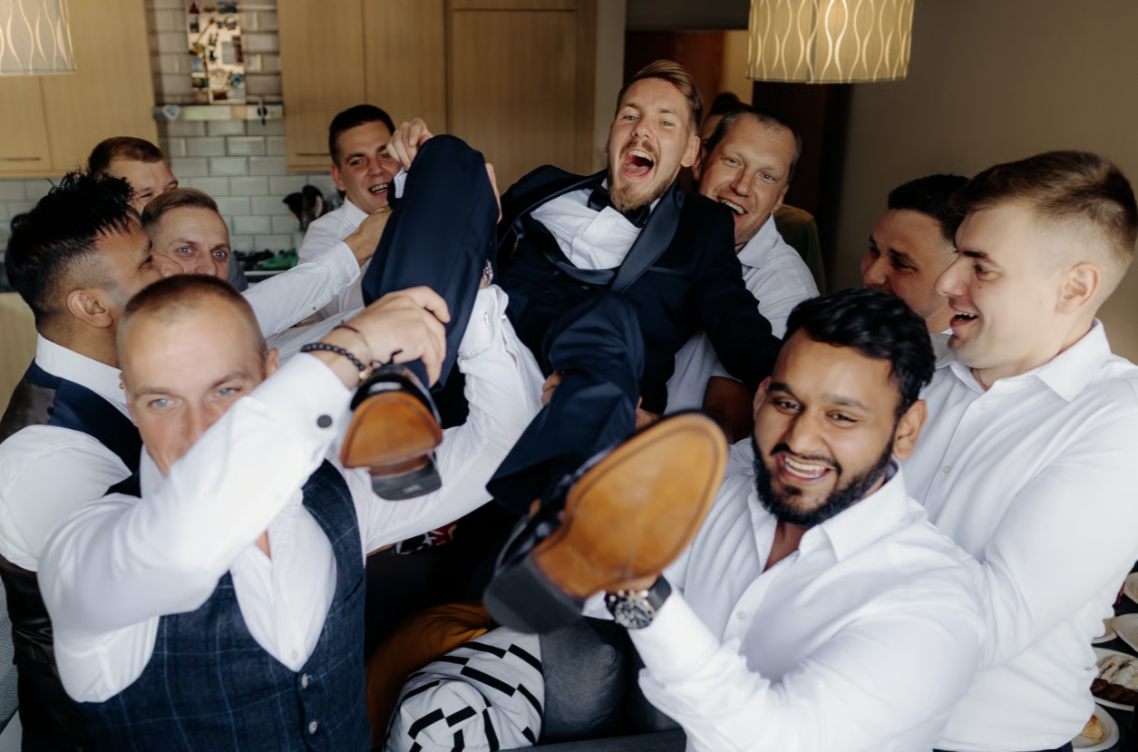 Groomsmen holding up groom in a playful manner during a wedding caught on camera by the videographer
