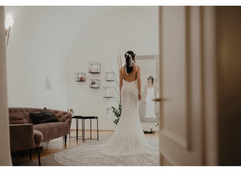 Braut bei der Brautkleid Anprobe mit langem Spitzenkleid vor dem Spiegel