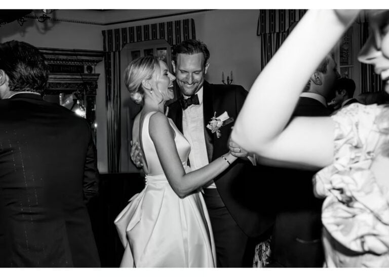 Ehepaar strahlt und tanzt auf der Hochzeitsfeier, umgeben von Gästen