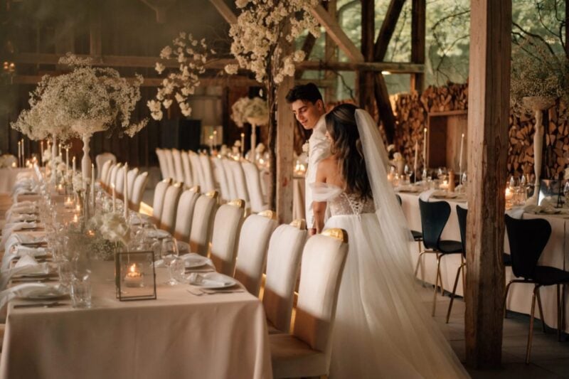 Brautpaar inspiziert glücklich die Dekoration im weiß und beige dekorierten Hochzeitssaal mit üppigen weißen Blumenelementen