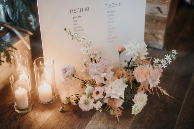 Sitzplan für die Hochzeit mit Tischordnung, Kerzen und romantischer Blumendeko auf Holztisch