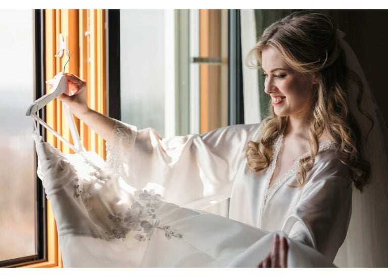 Braut beim Getting Ready am Hochzeitstag mit ihrem Brautkleid am Fenster