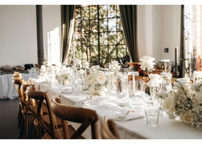 Festlich gedeckte Hochzeitstafel mit weißen Blumen und großen Fenstern im Hintergrund