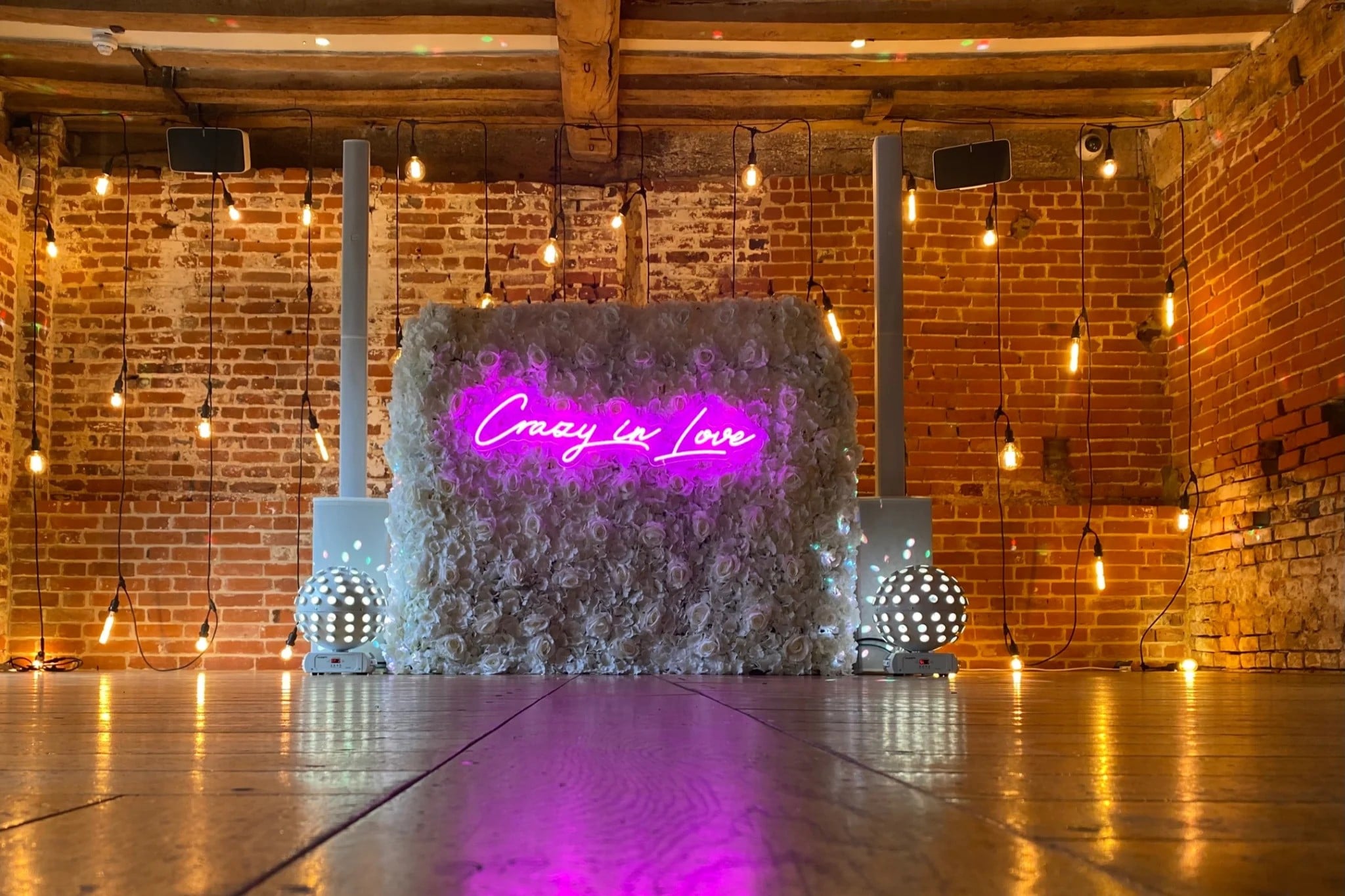 A dance floor set up a wedding with a floral wall and a crazy in love neon light