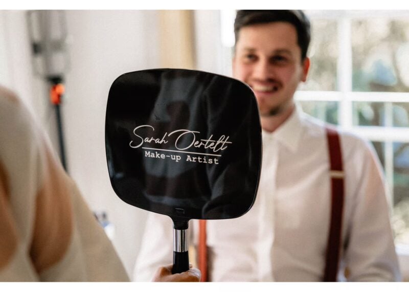 Bräutigam lächelt beim Getting Ready am Hochzeitstag während ein Styling Spiegel im Vordergrund steht