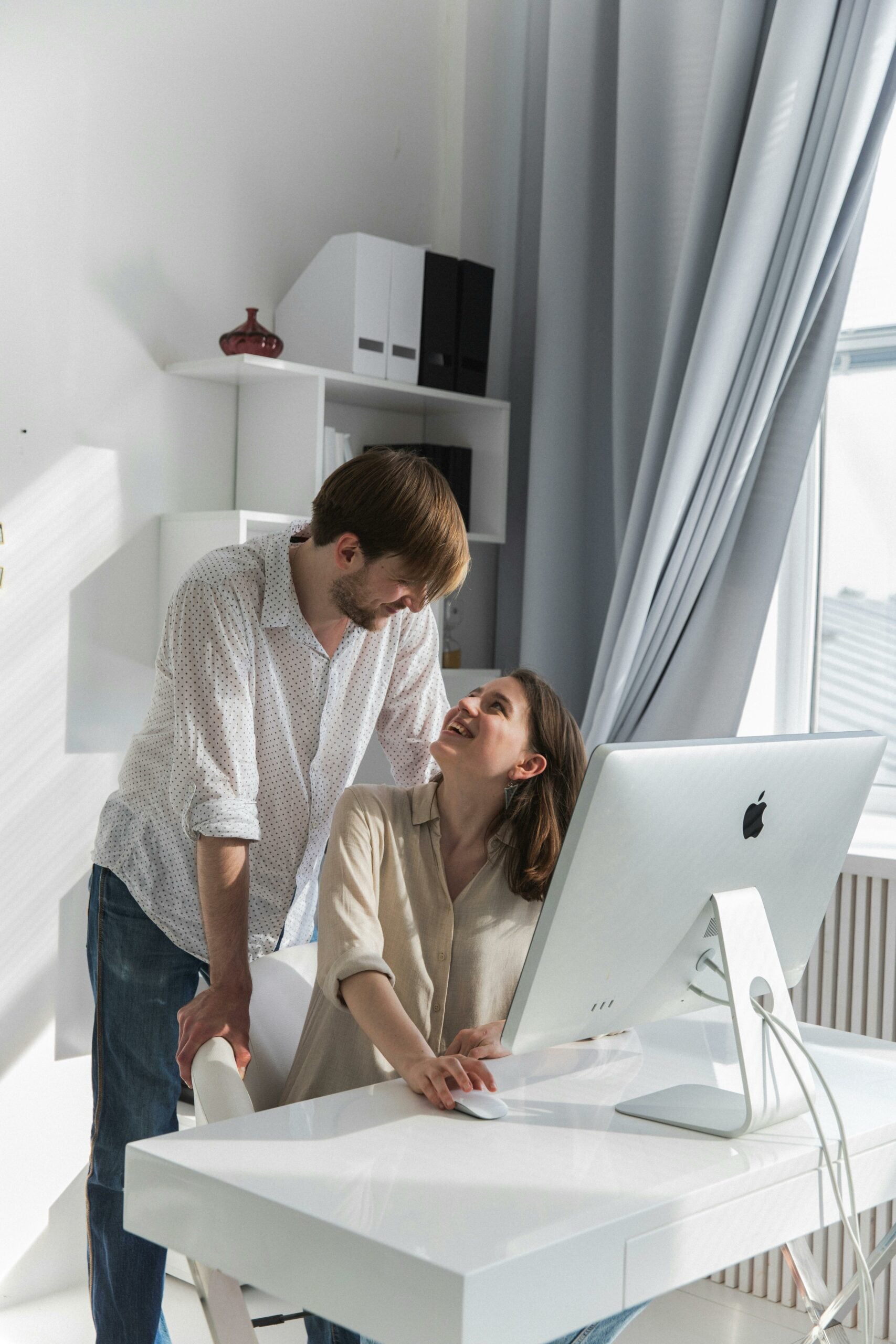 Engaged couple smiling as they create a wedding website on a mac