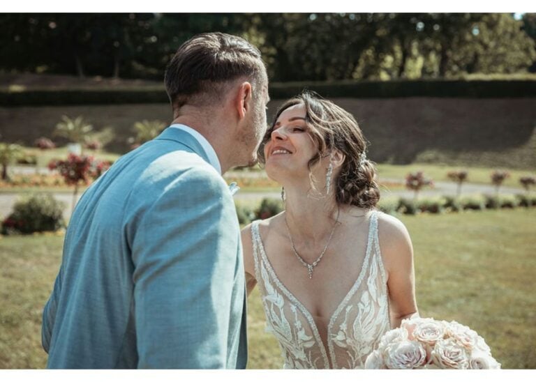 Braut und Bräutigam lächeln sich im Garten an, die Braut hält einen Rosenstrauß