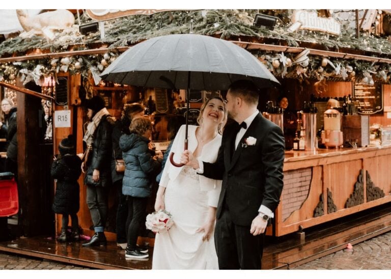 Braut und Bräutigam stehen mit einem Regenschirm vor einem Weihnachtsmarktstand